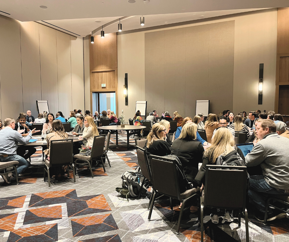 A large conference room filled with round tables and groups of people engaged in discussion.