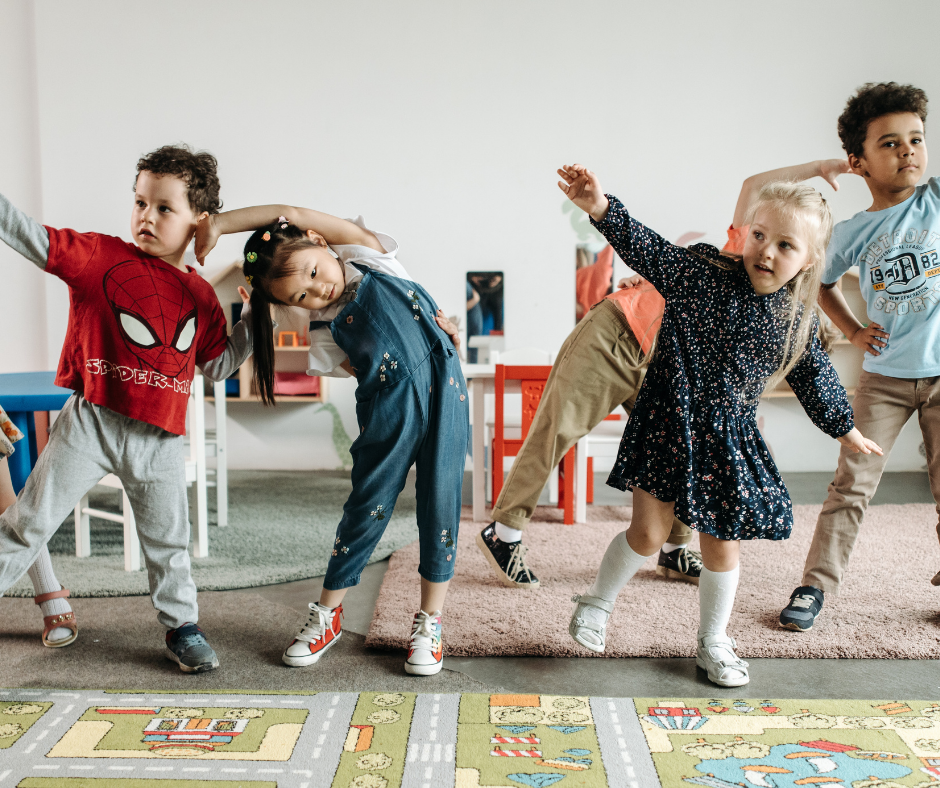 Group of young children dancing and stretching in a classroom or playroom.