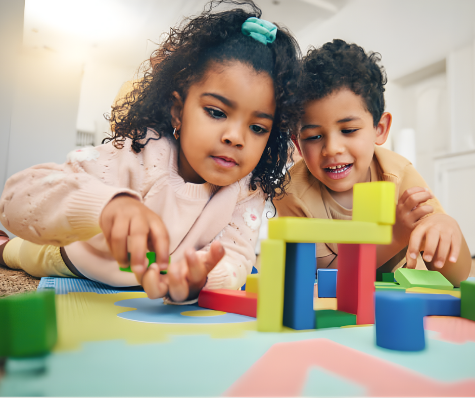 Two young children playing with colorful building blocks on the floor indoors.