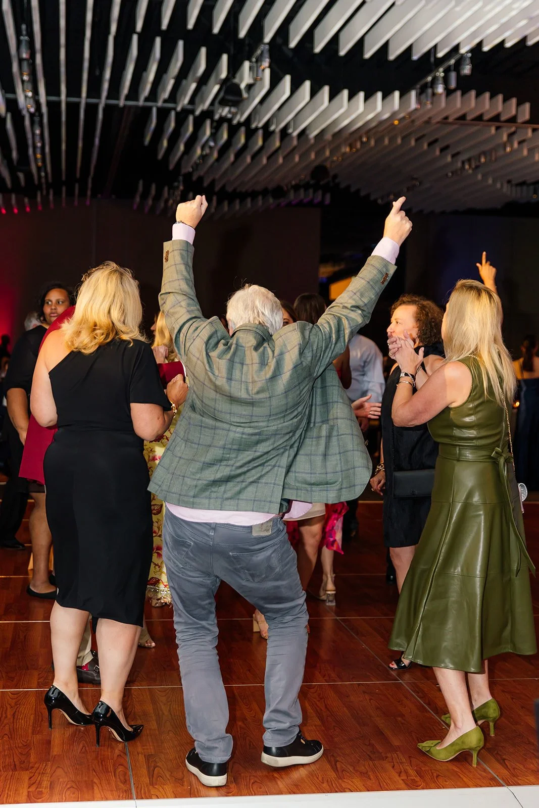 People dancing and celebrating at an event, with a man in a green plaid blazer raising his arms.