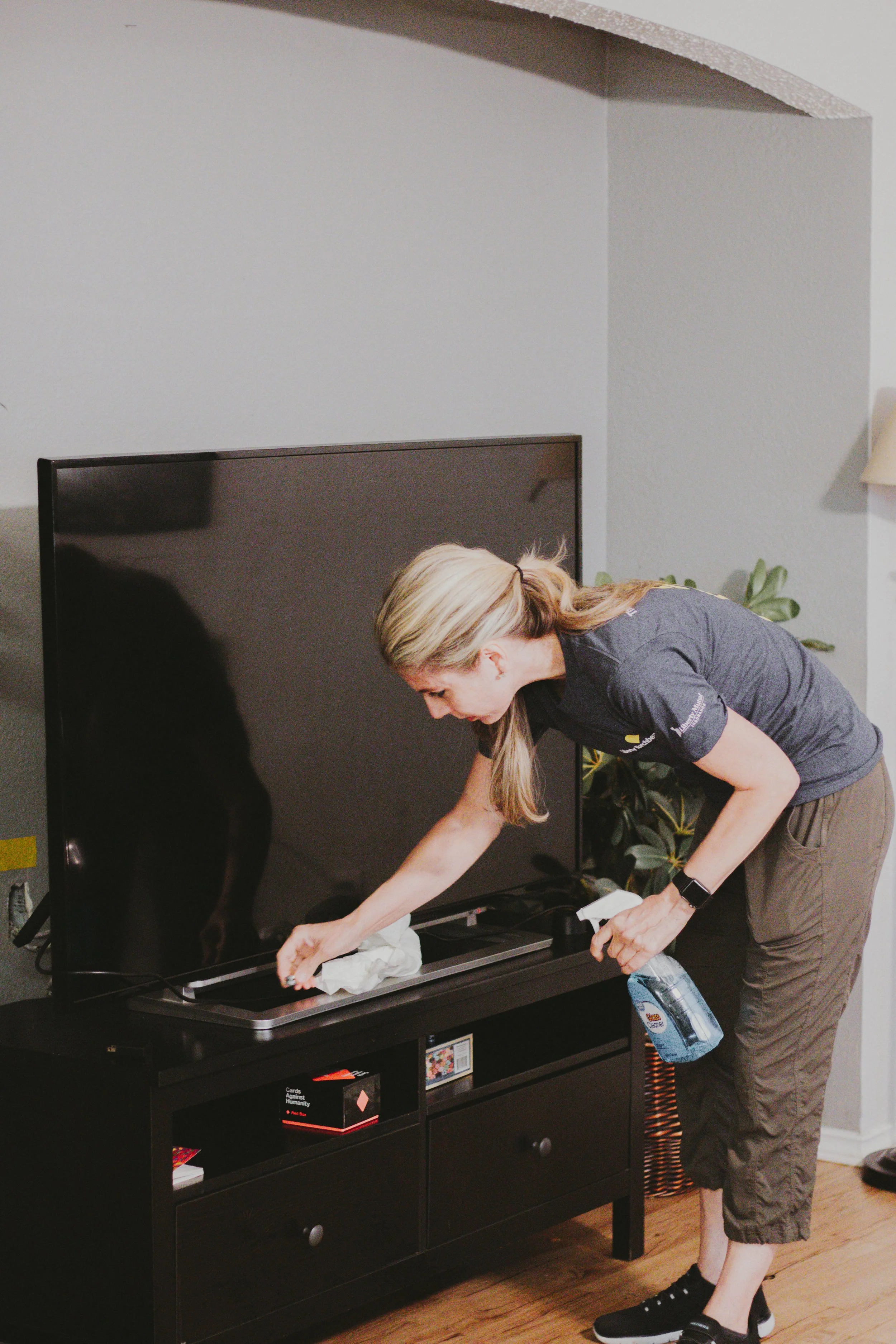 A woman cleaning a large flat-screen TV in a living room.