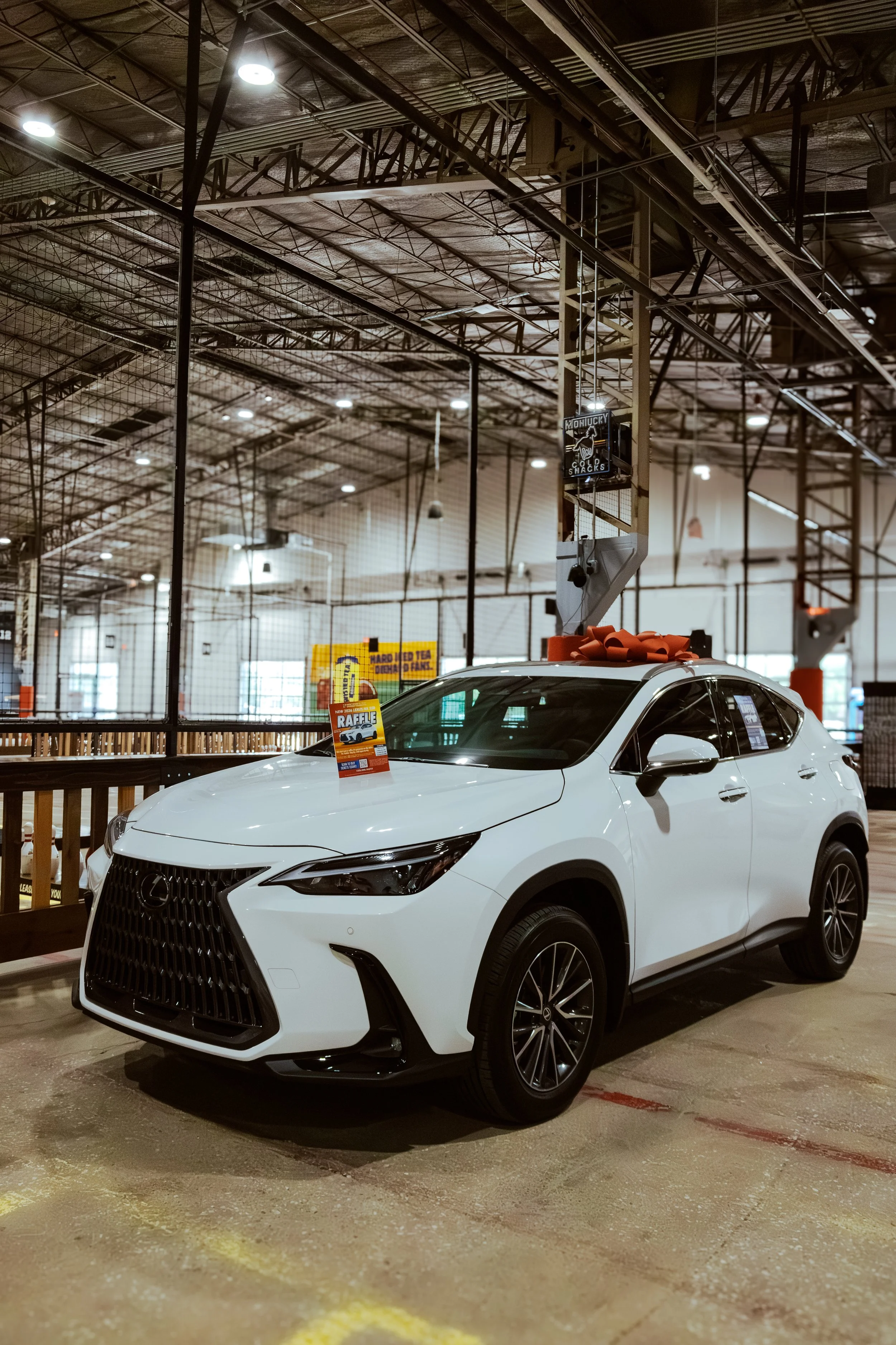 White Lexus SUV displayed indoors with a large red bow on top promoting the CUTX Lexus Car Raffle benefiting local nonprofits including City House.