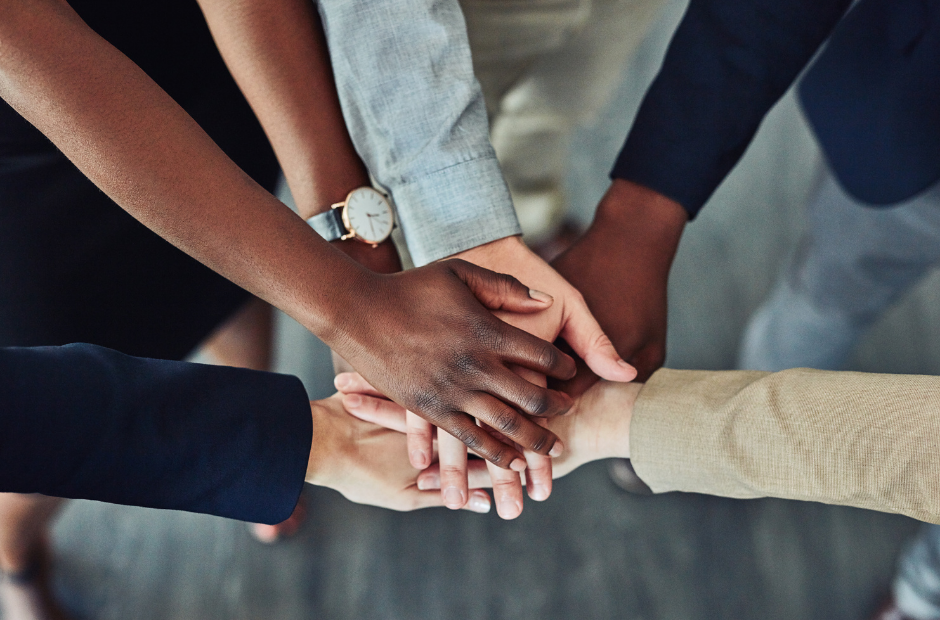 Multiple people of diverse backgrounds stacking their hands together in a show of unity and teamwork.
