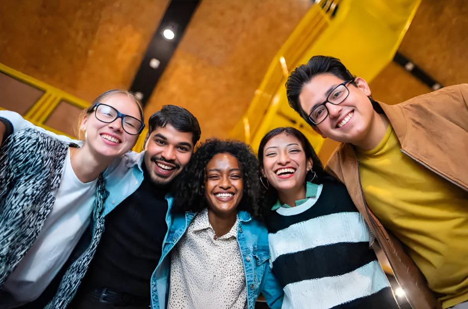 Group of five young people smiling and posing together indoors.