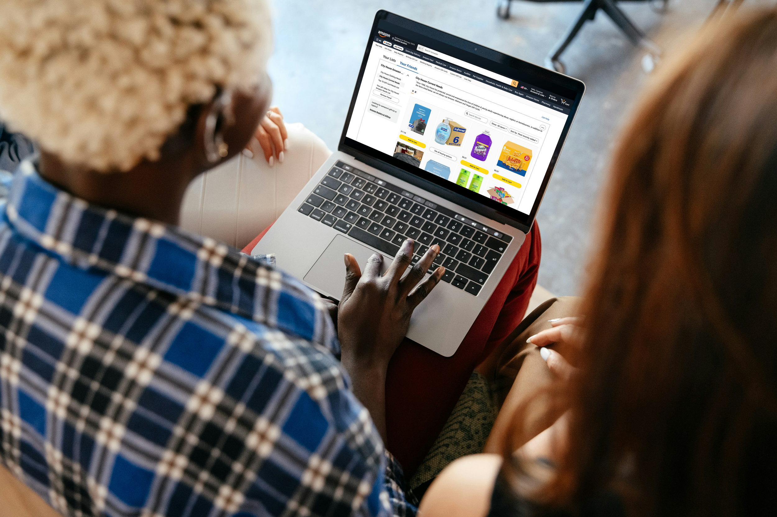 Two women browsing Amazon online shopping website on a laptop, sitting close together.