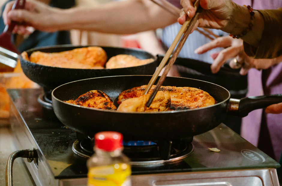 People cooking and flipping food in frying pans on a stovetop.