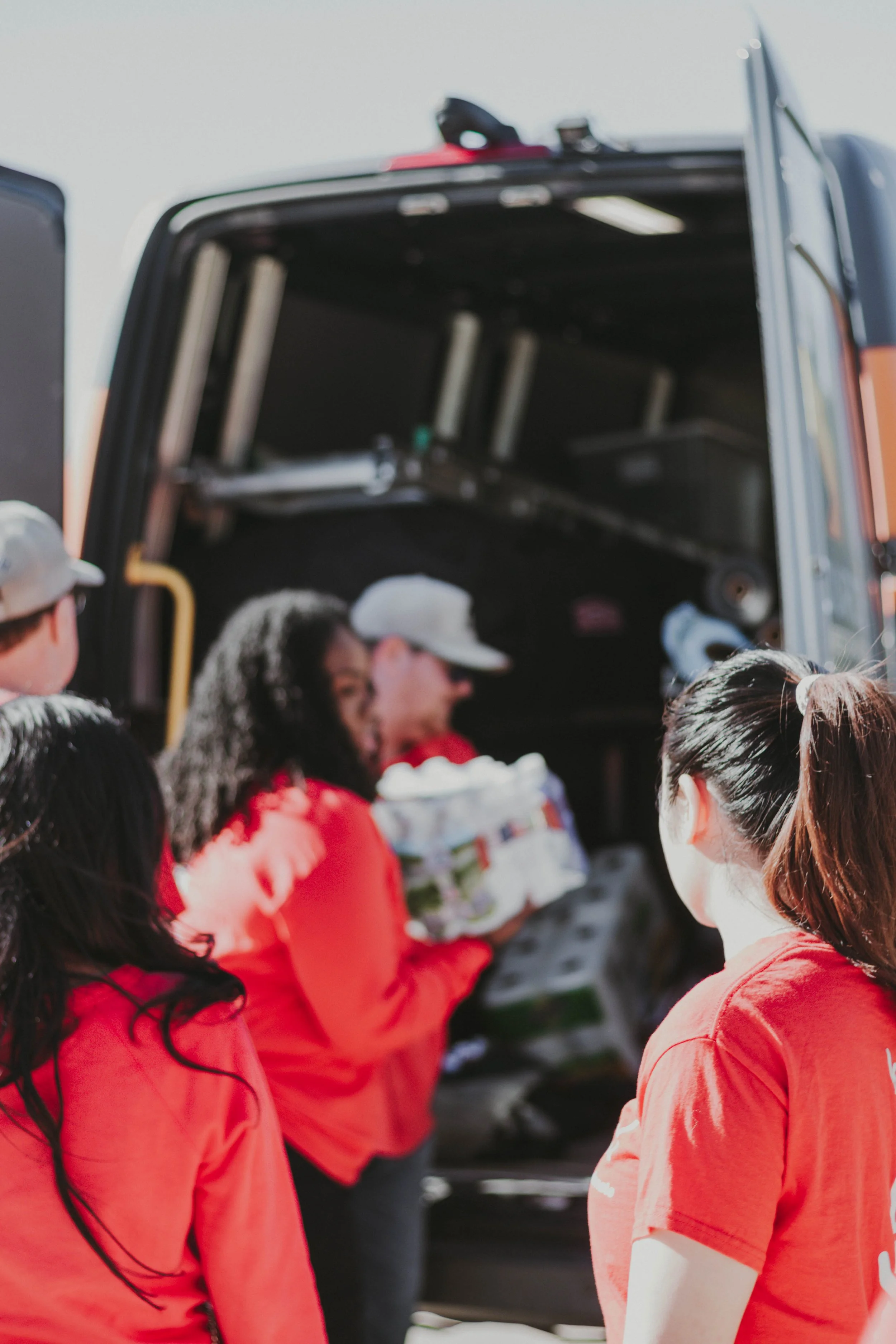 A group of people wearing red shirts are loading supplies into a van with its door open.