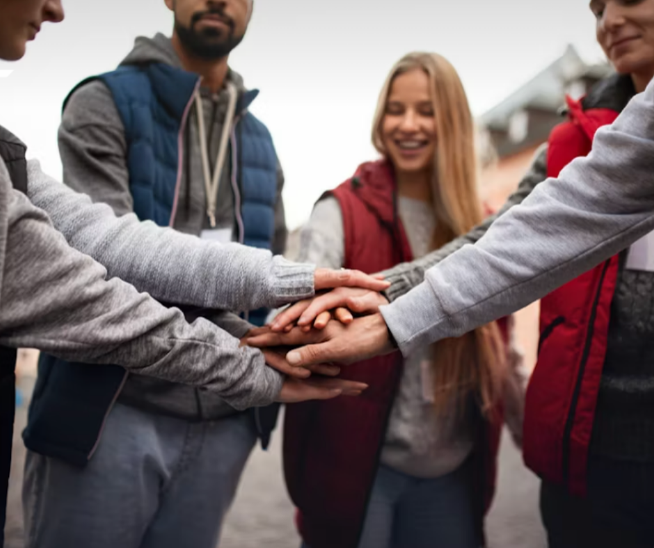 Group of young people placing hands together in a show of teamwork outdoors