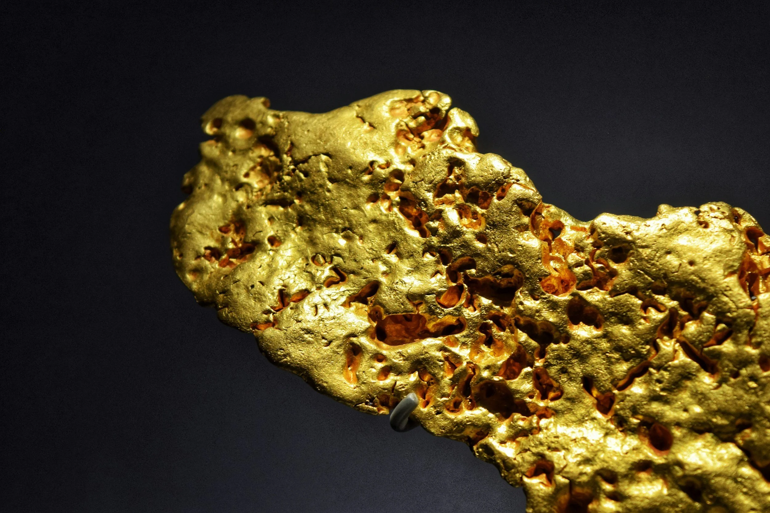 Close-up of a gold nugget with a porous, irregular surface against a black background.