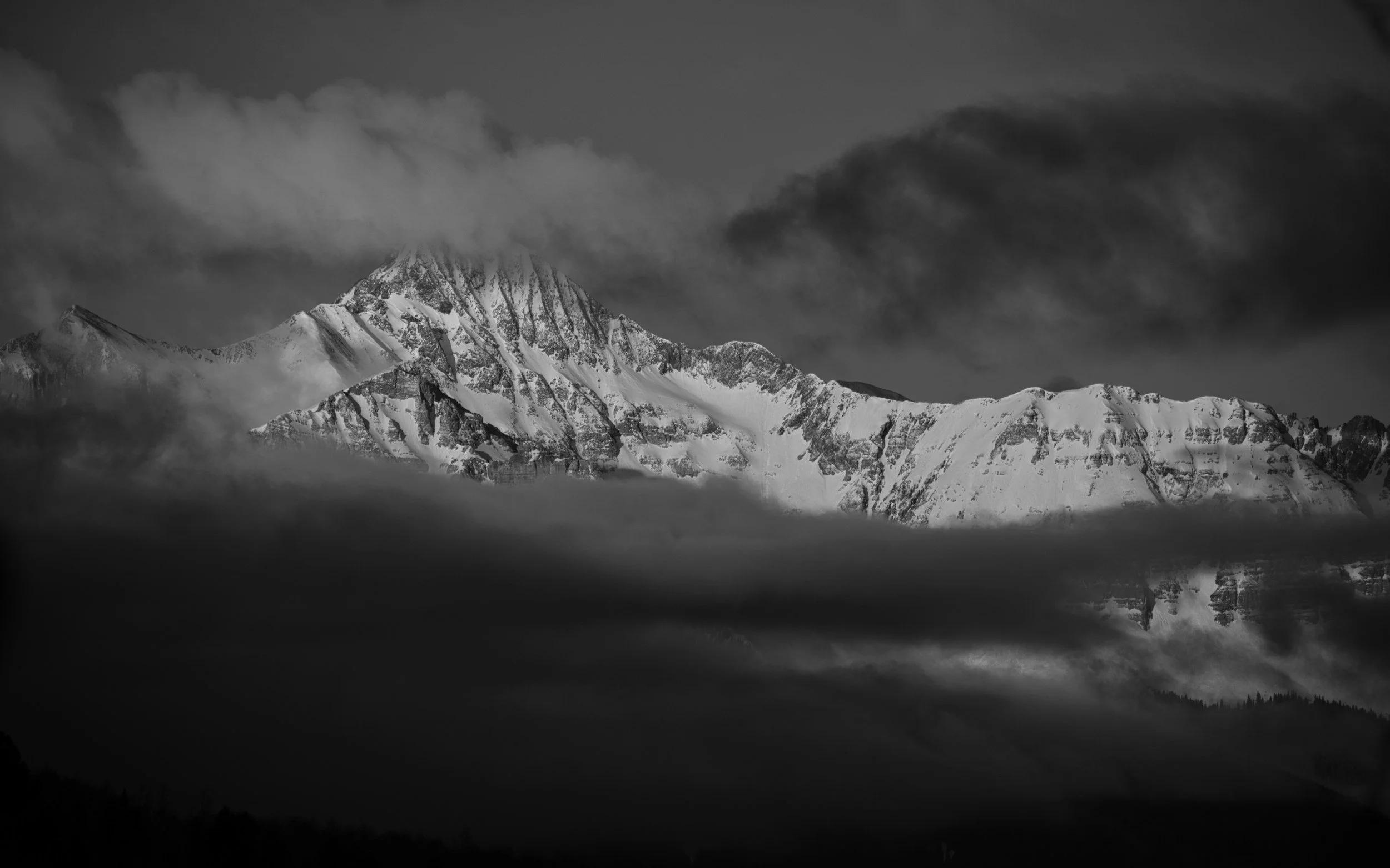 Black and white photograph of a snow-capped mountain with clouds around the peak.