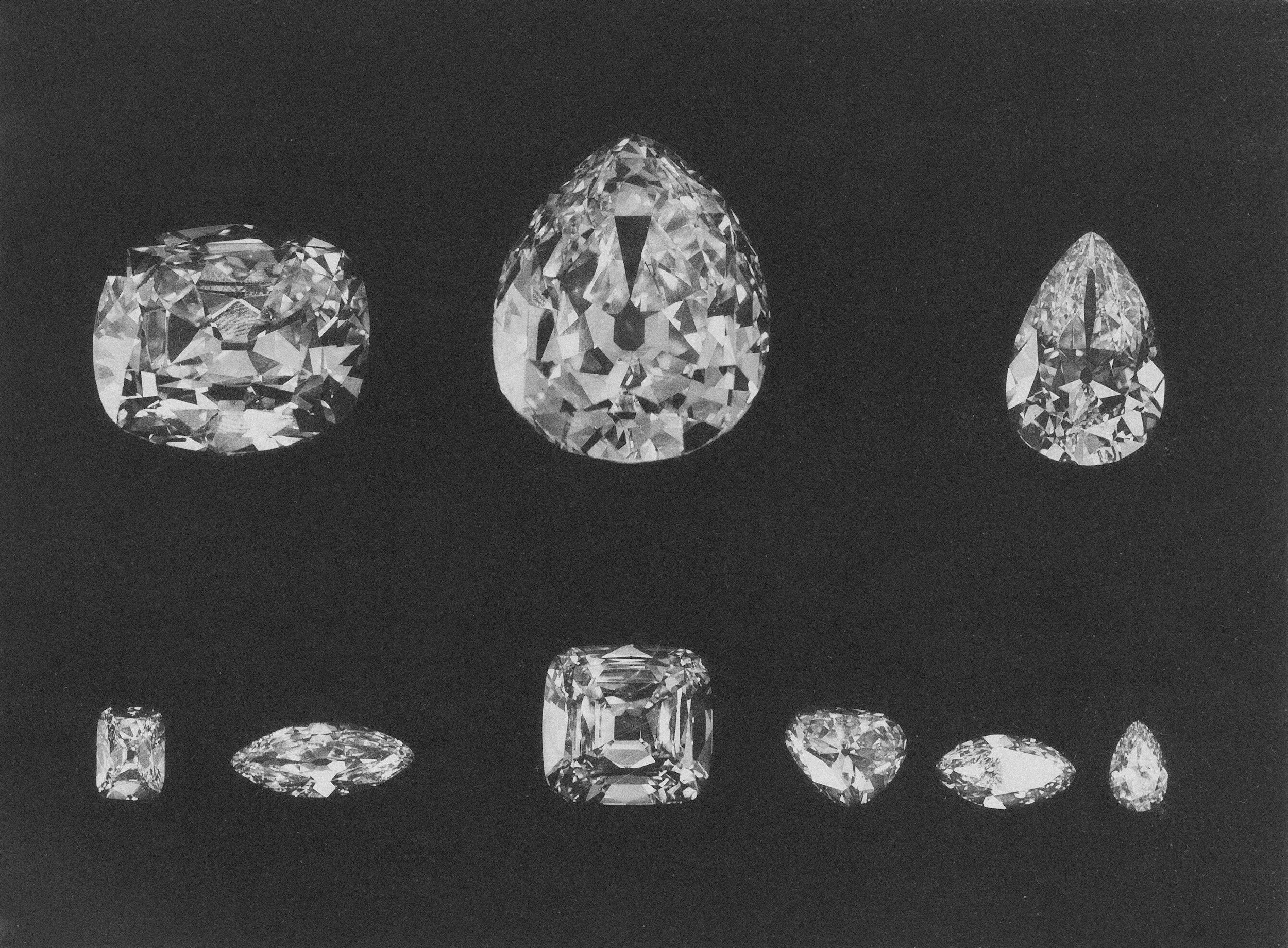 Multiple diamonds of various cuts and sizes displayed against a dark background, arranged in two rows with larger diamonds on top and smaller on bottom.
