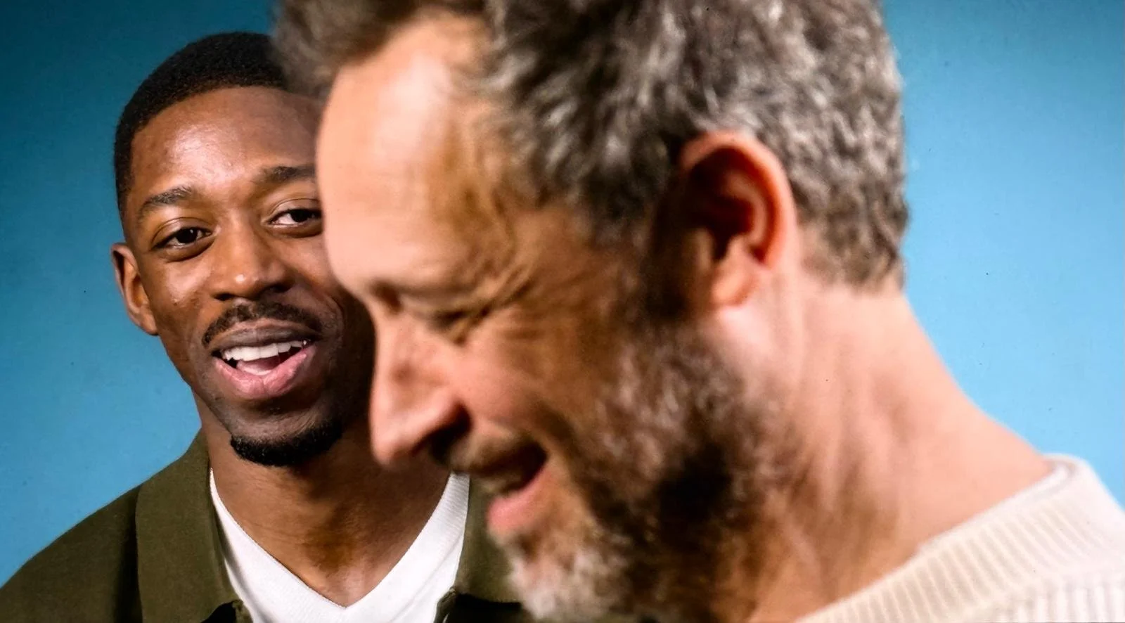 Deux hommes ayant une conversation, un homme dit quelque chose en souriant envers un autre homme dont le visage est en partie visible.