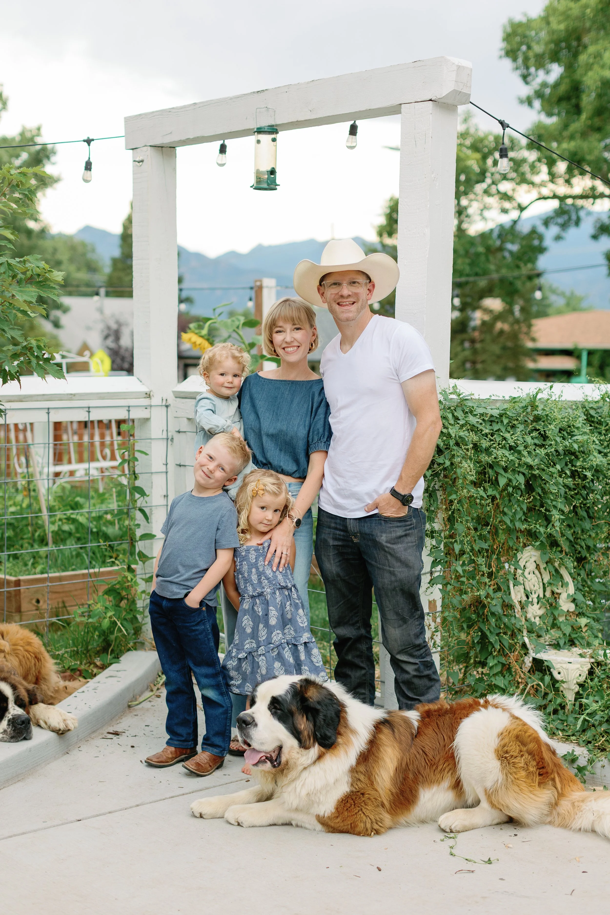 Shobie Spear's family portrait with three children, two adults, and dogs in a garden with a mountain background.