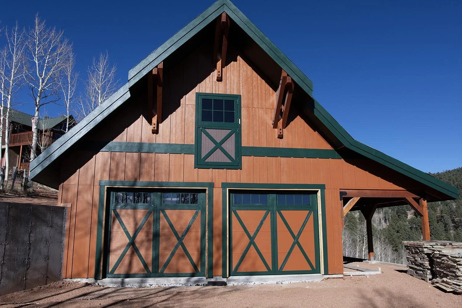 Front view of a barn-style wooden house with green accents, a sloped roof, and a large double garage door.