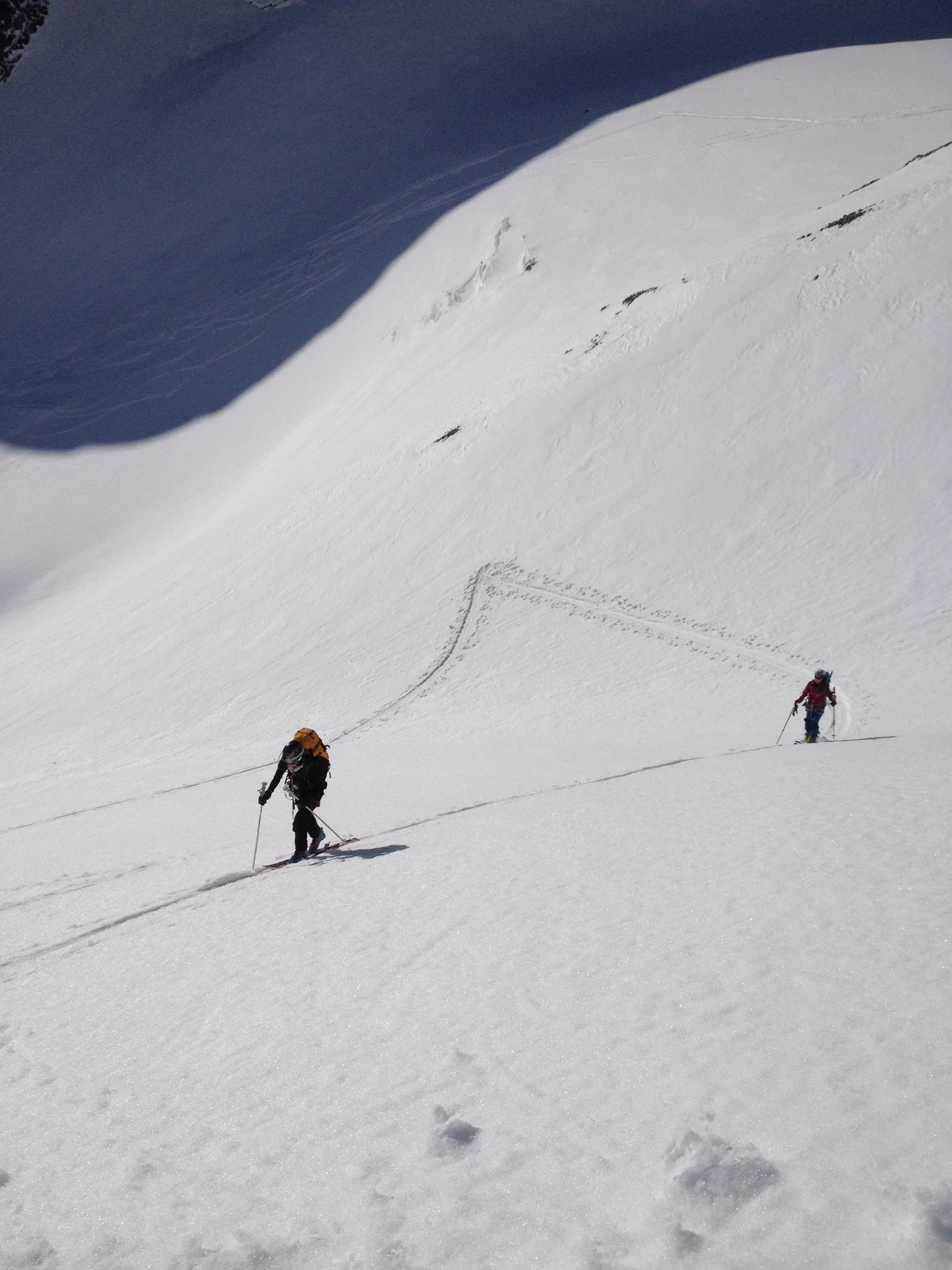 Deux skieurs traversent une neige poudreuse dans un paysage montagnard ensoleillé.