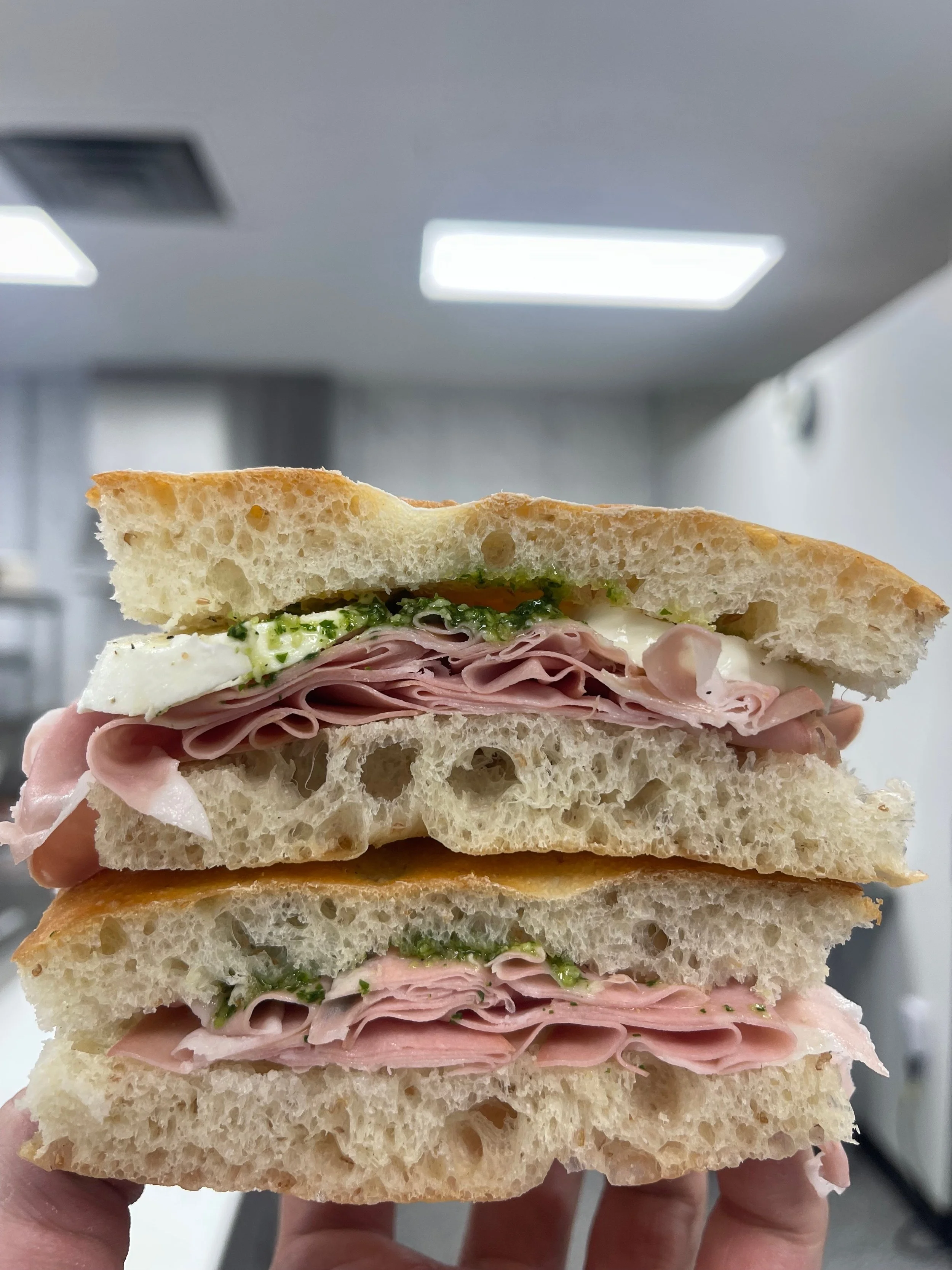 Close-up of a stacked ham and turkey sandwich on white bread, with lettuce, cheese, and green sauce inside.