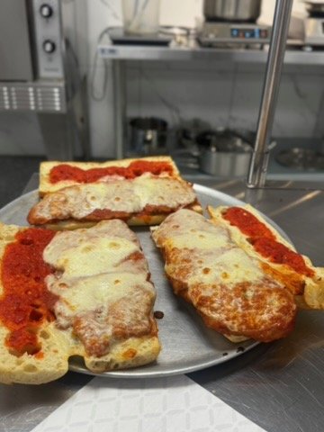 Three gourmet sandwiches on a metal tray in a kitchen.