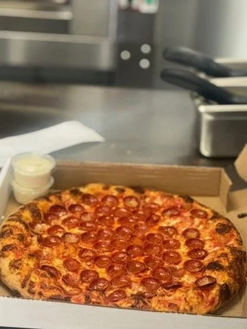 Pepperoni pizza in a cardboard box on a counter in a kitchen.