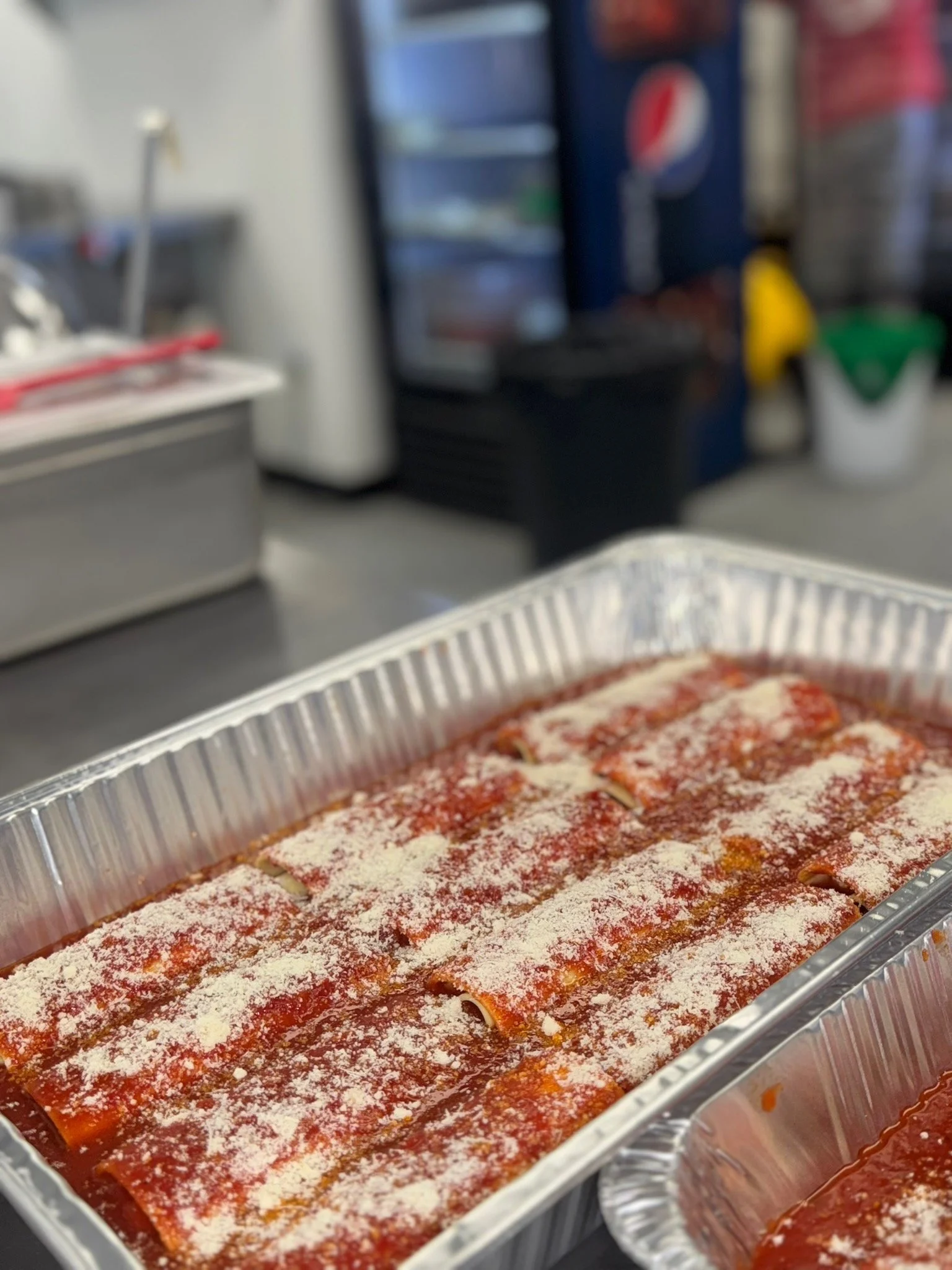 Tray of uncooked lasagna with tomato sauce and cheese.