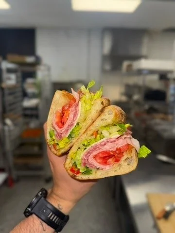 Close-up of a hand holding a sandwich with lettuce, tomato, turkey, and bread inside.