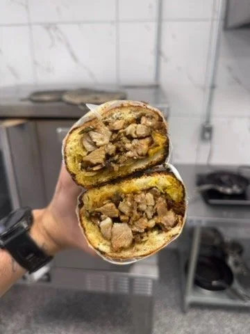 Halved meat-filled sandwich with bread and visible cooked meat inside.