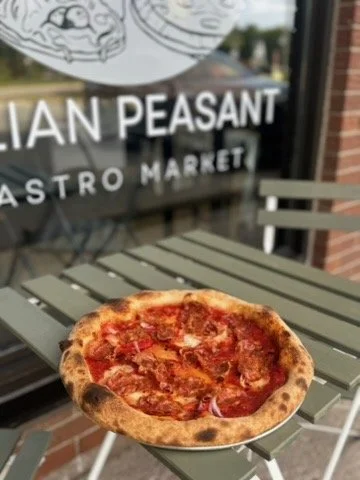 A pizza with pepperoni and toppings on a table outside a restaurant.