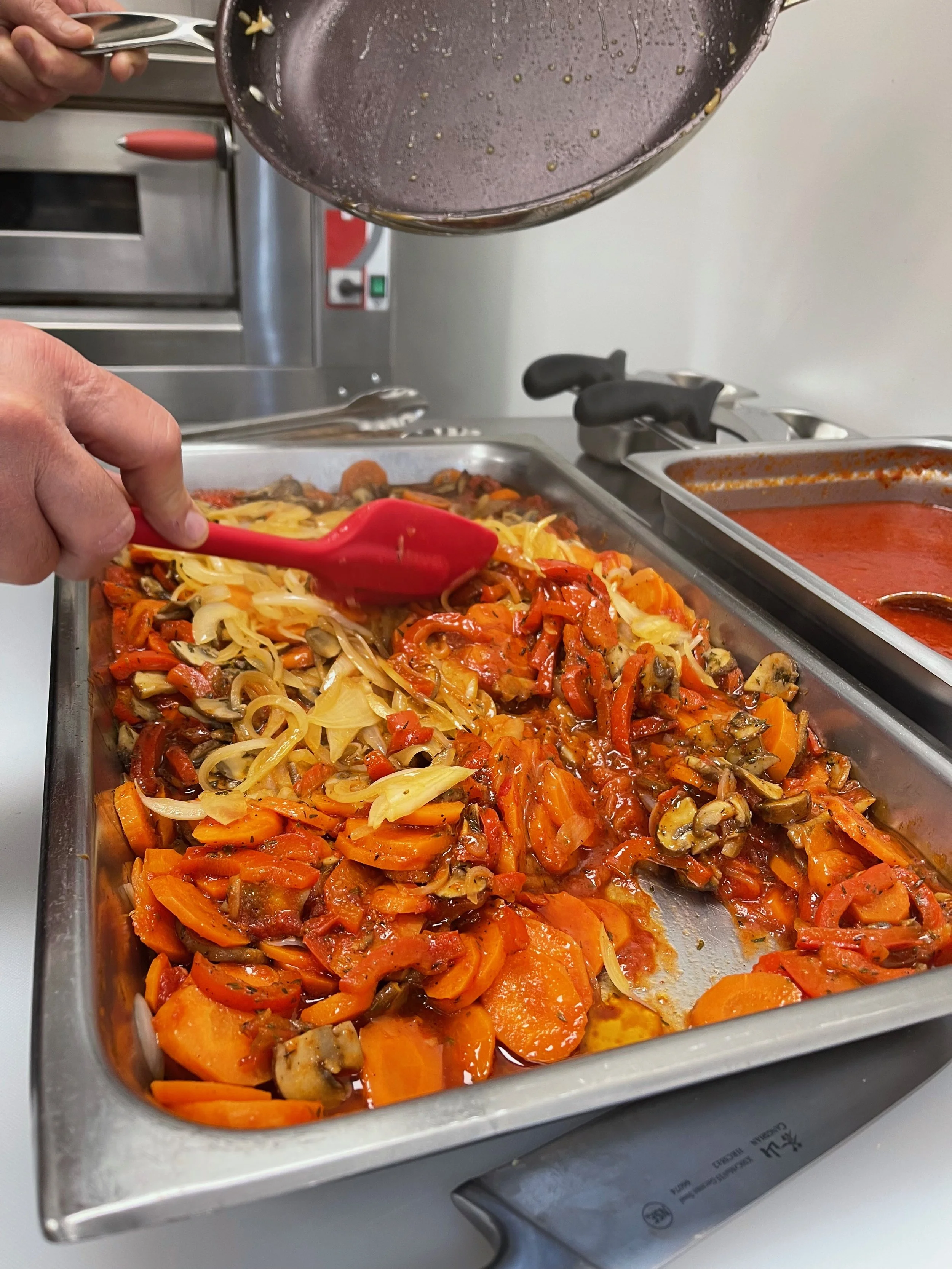 Serving tray of cooked vegetables, including carrots, onions, peppers, and mushrooms in a kitchen.