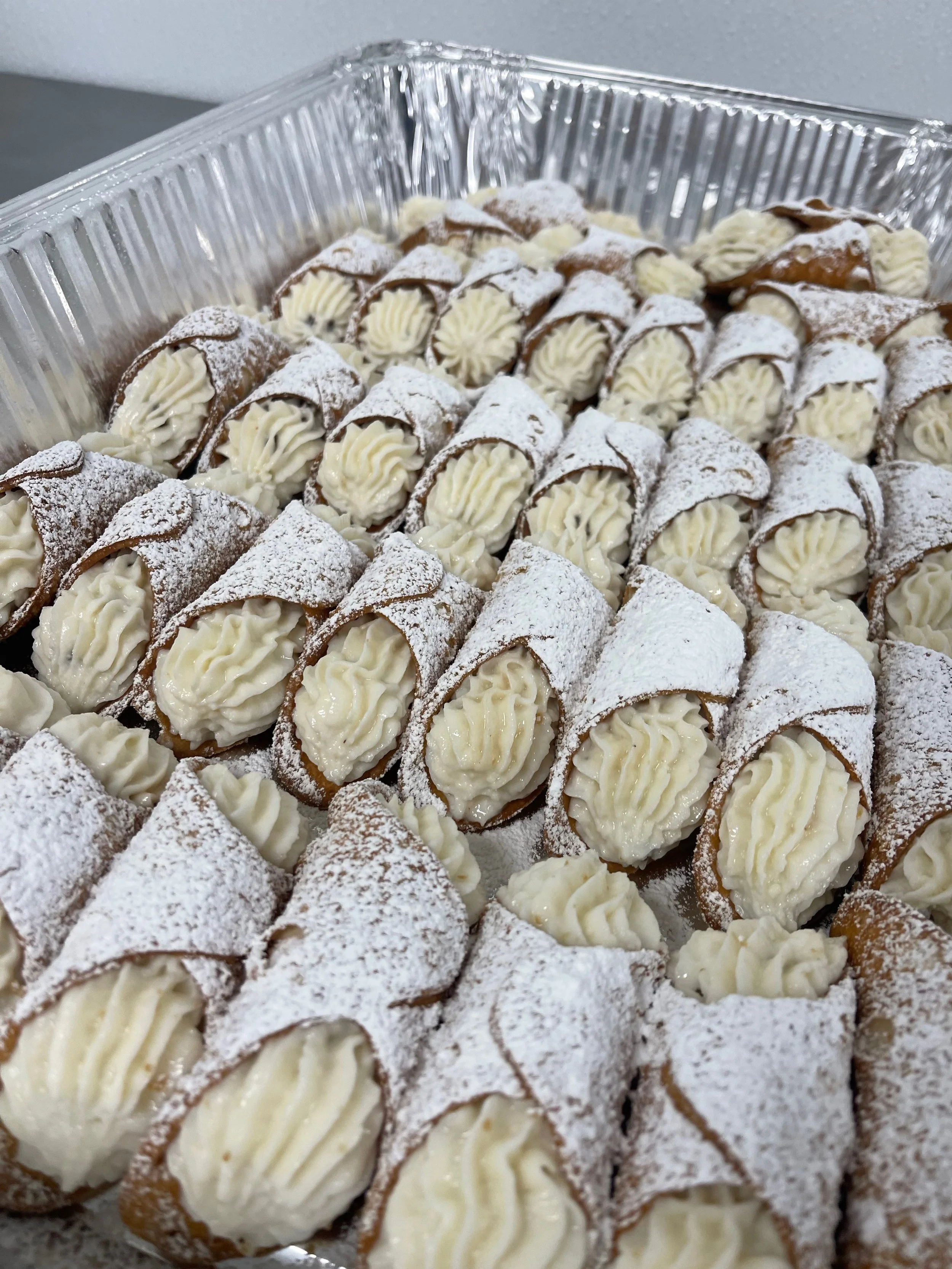 Tray of cannoli desserts dusted with powdered sugar, filled with creamy white filling.