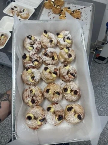 Tray of cream-filled pastries topped with powdered sugar and small dollops of cream and blueberries.