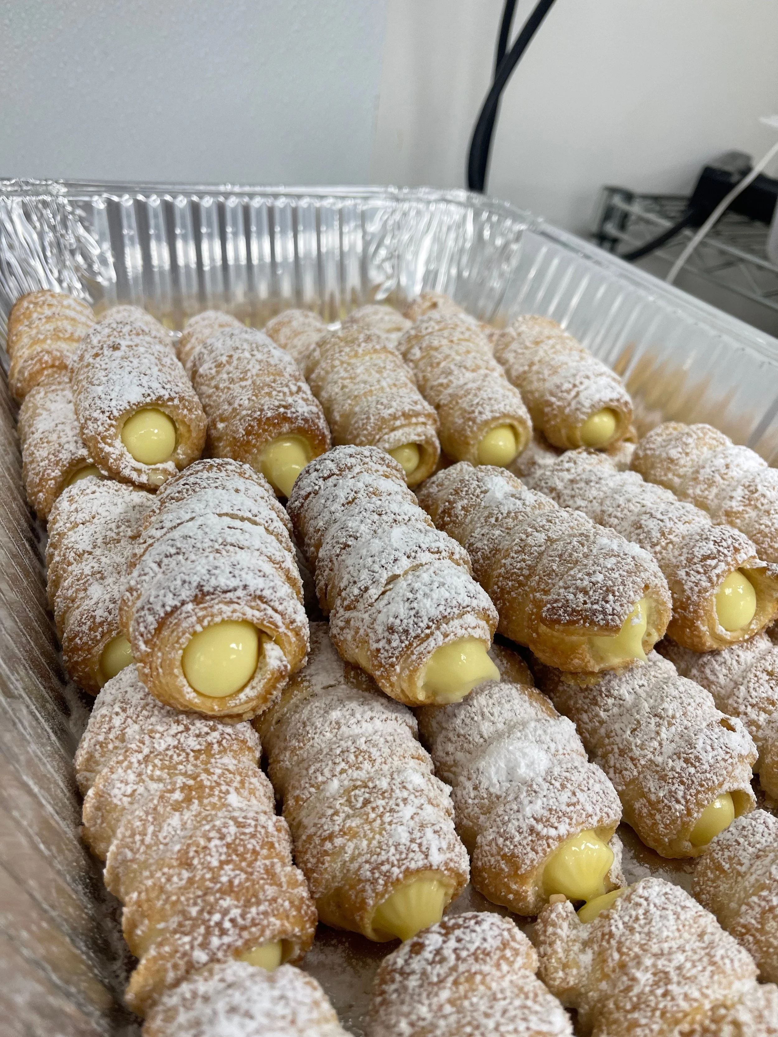 Tray of cannoli pastries dusted with powdered sugar, filled with creamy filling.
