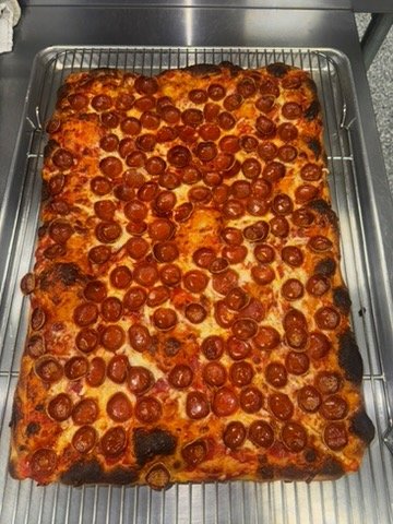 Baked rectangular pepperoni pizza on cooling rack.