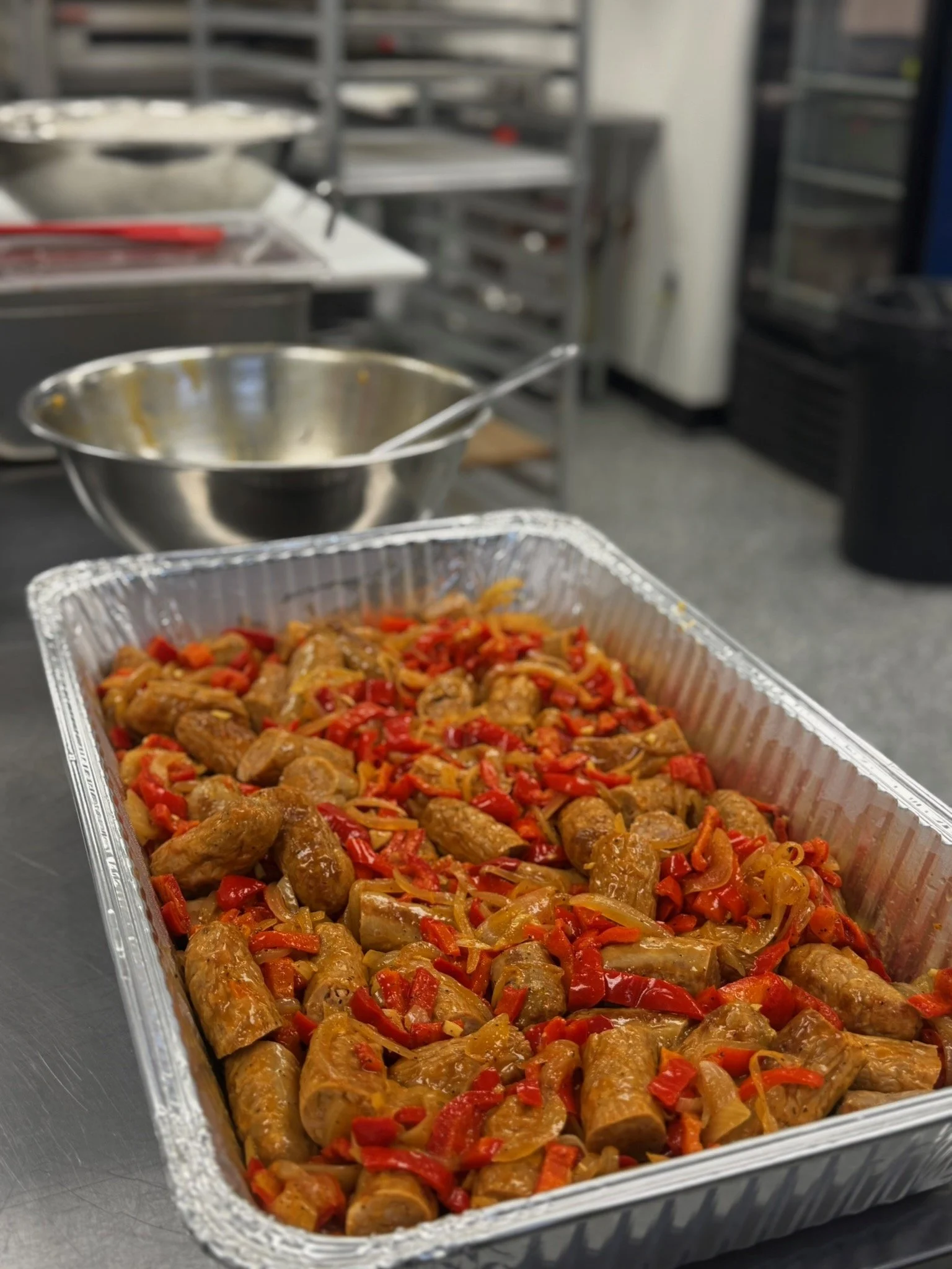 Tray of cooked sausage and peppers in a commercial kitchen setting.