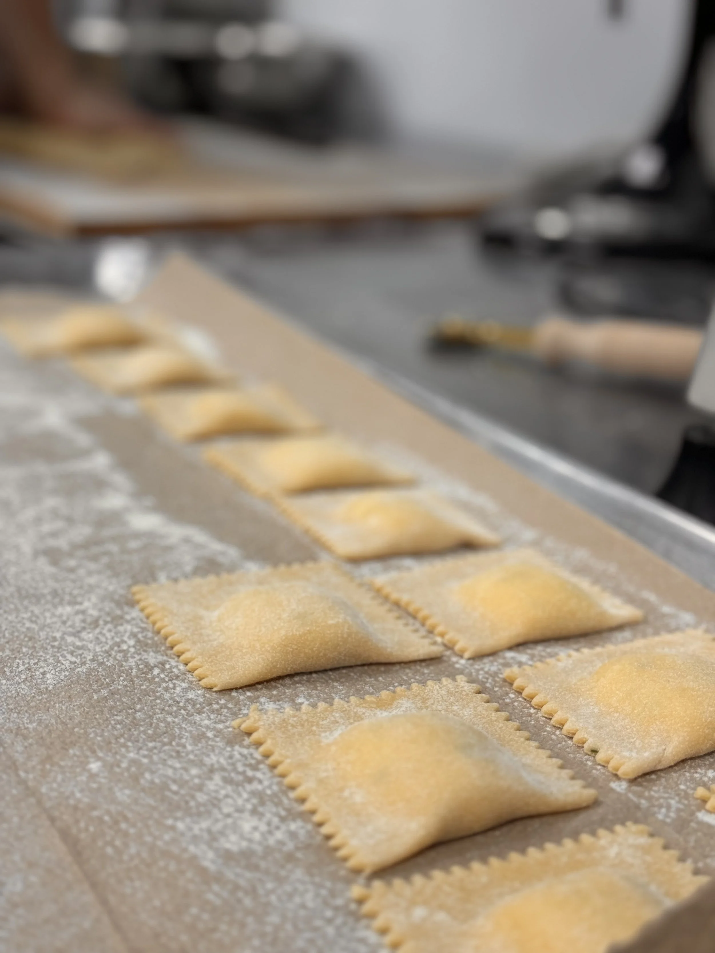 Several uncooked ravioli pasta pieces on a floured surface.