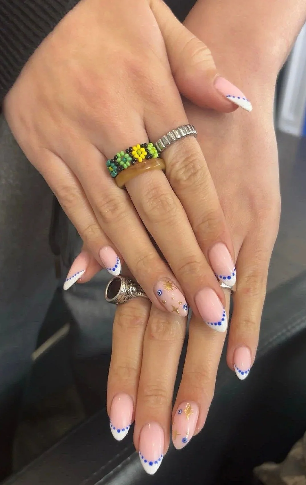 Close-up of hands with colorful rings and manicured nails featuring a blue and white design, and gold star and eye decorations.