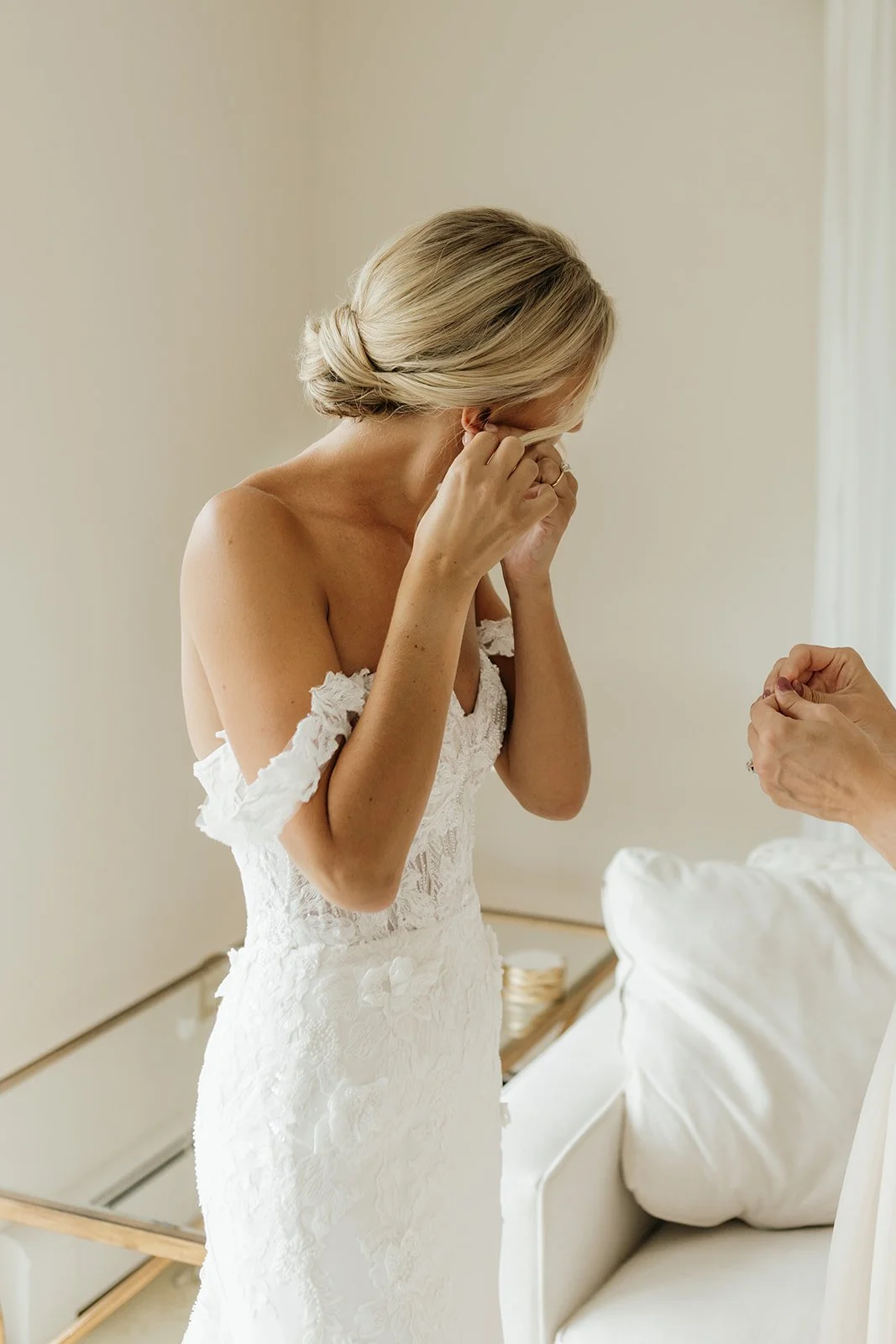 A woman in a white wedding dress is crying while someone else places a ring on her finger.