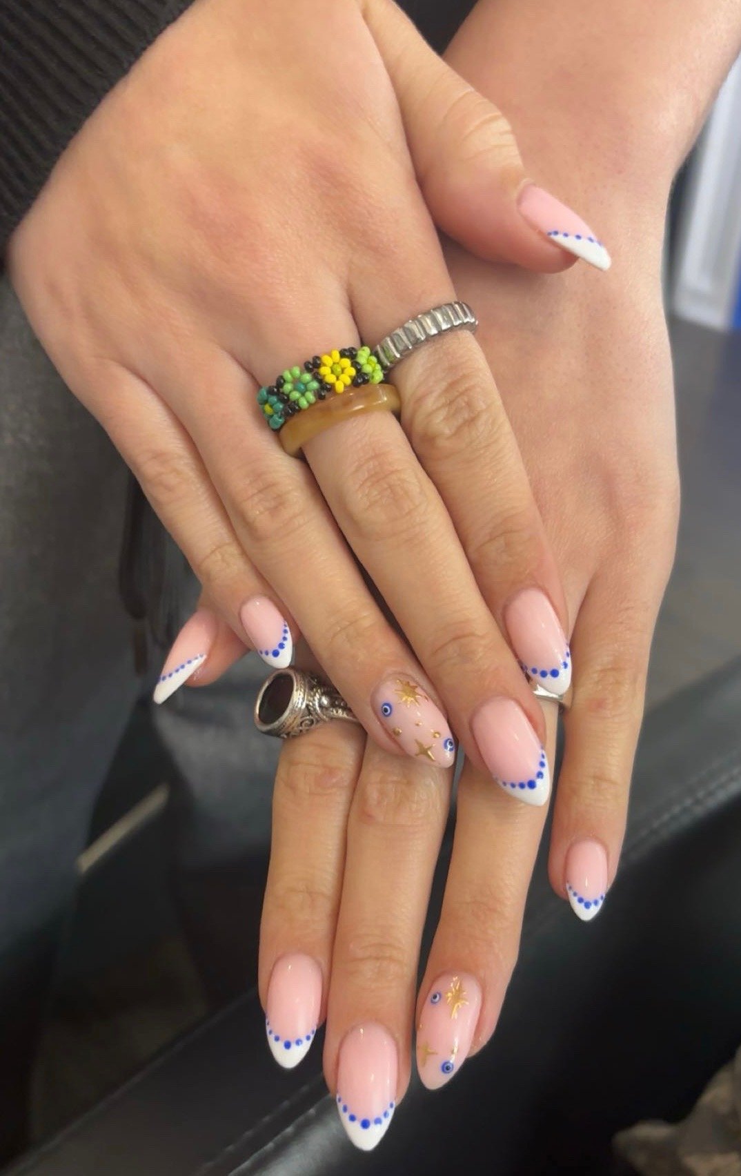 Close-up of hands with colorful rings and manicured nails featuring a blue and white design, and gold star and eye decorations.