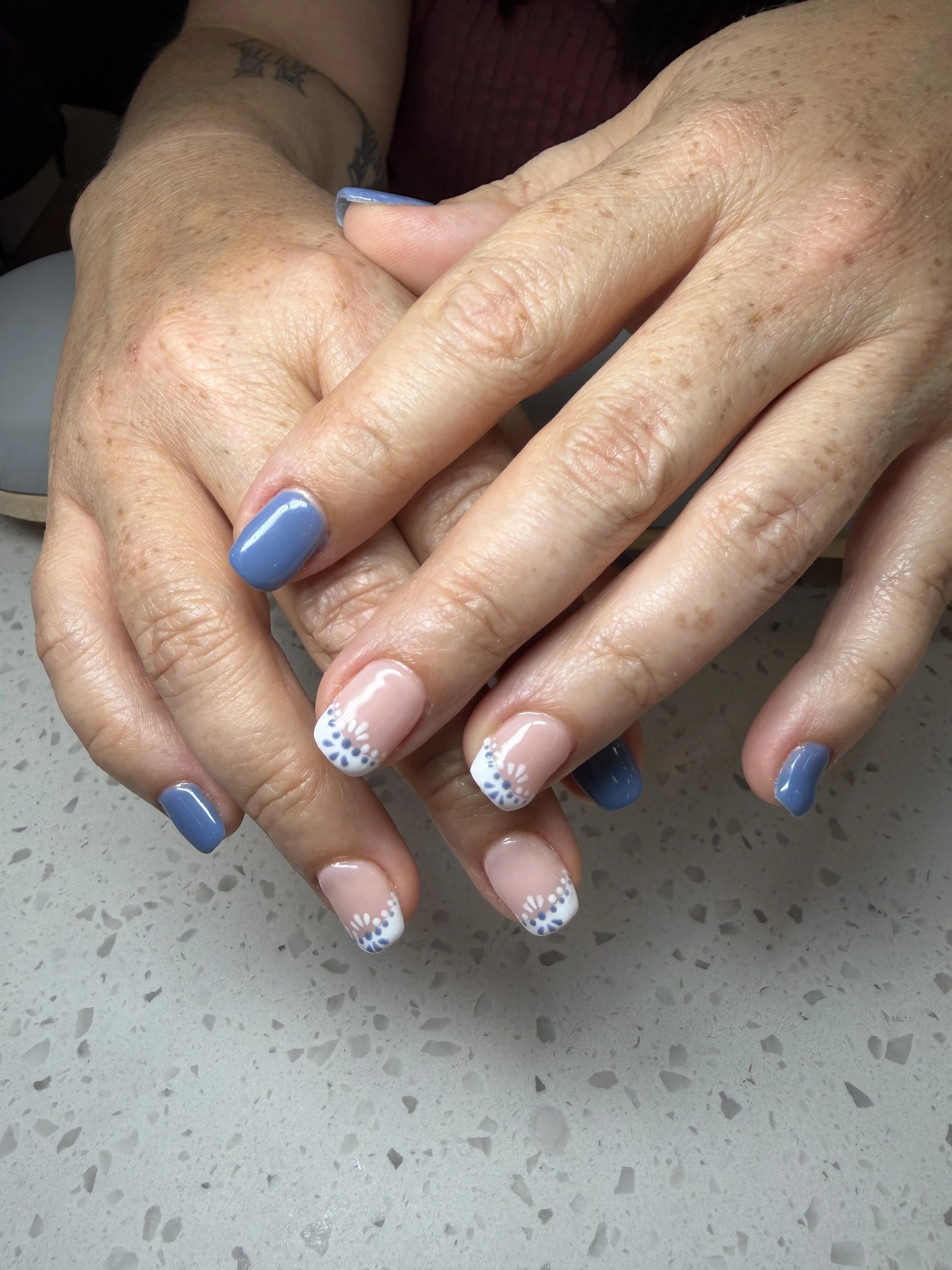 Close-up of two hands with manicured nails, one with blue polish and the other with a French tip design, resting on a speckled countertop.
