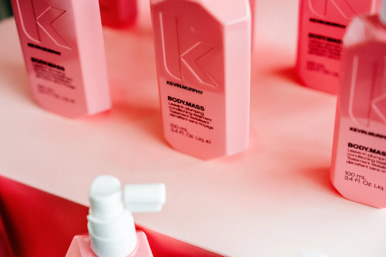 Pink bottles of body mass and a white pump bottle on a pink surface.