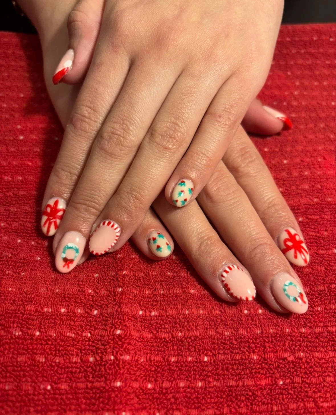 Close-up of hands with holiday-themed manicured nails resting on a red textured surface.