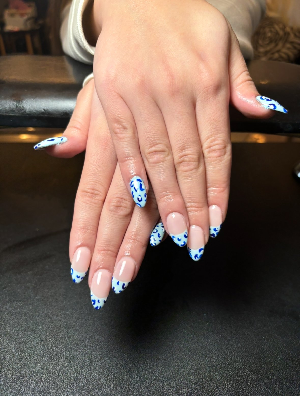 Hands with blue and white leopard print nail polish resting on a black surface.