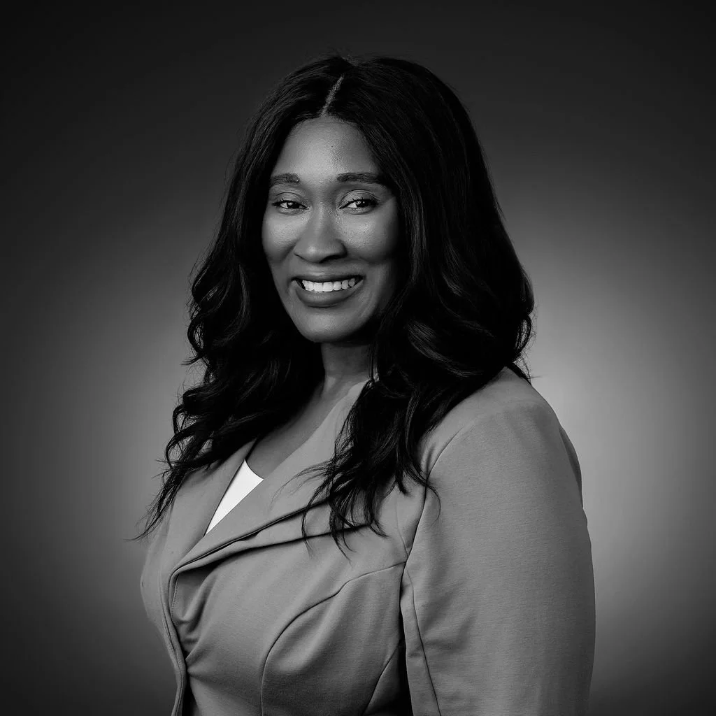 Black and white professional portrait of a woman with shoulder-length wavy hair, smiling, wearing a blazer.