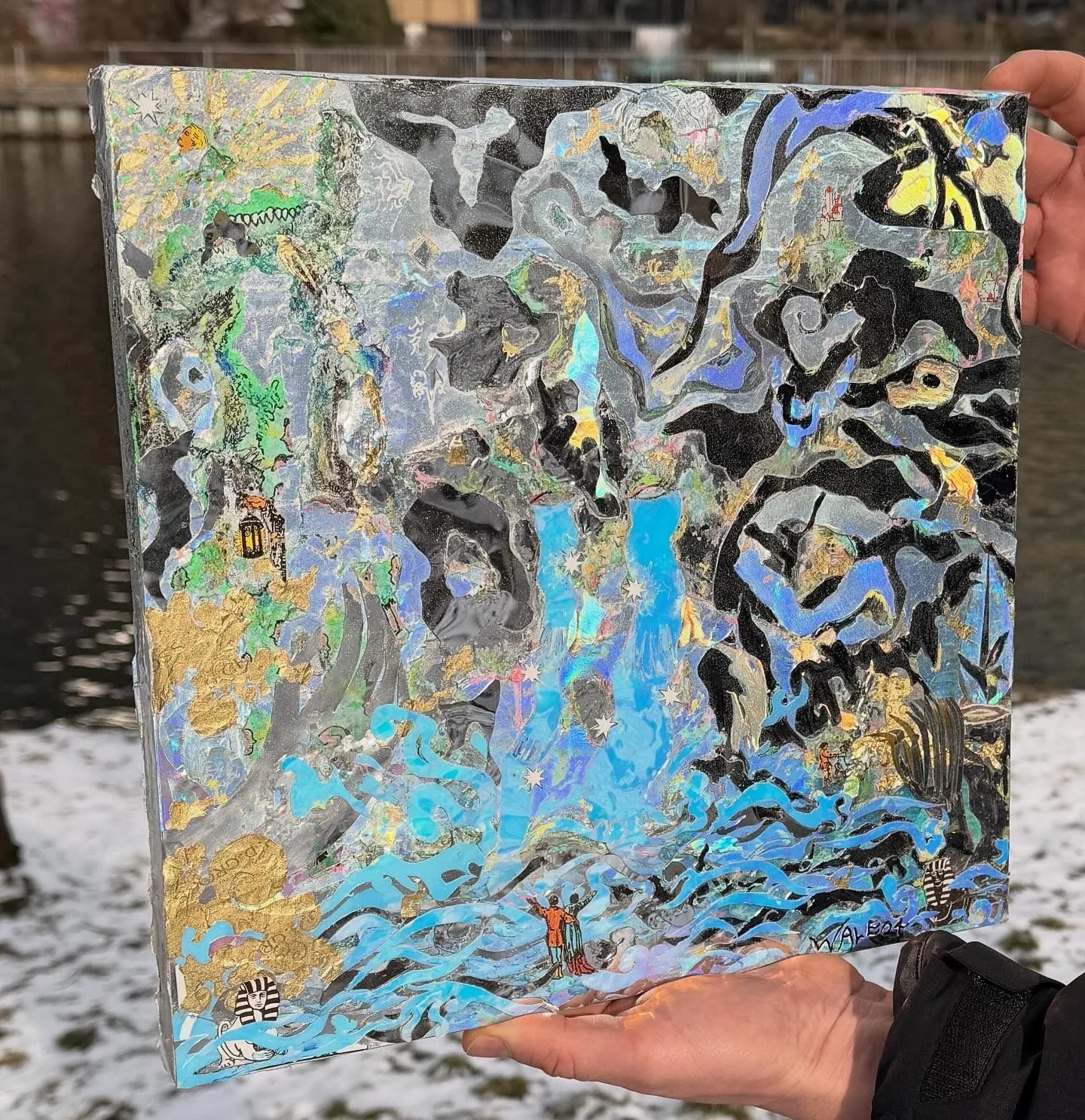 Mapa artístico y colorido con ríos, cascadas, figuras humanas, animales y elementos naturales. Incluye detalles en dorado y colores brillantes. Está siendo sostenido por una mano en un fondo de agua y nieve.