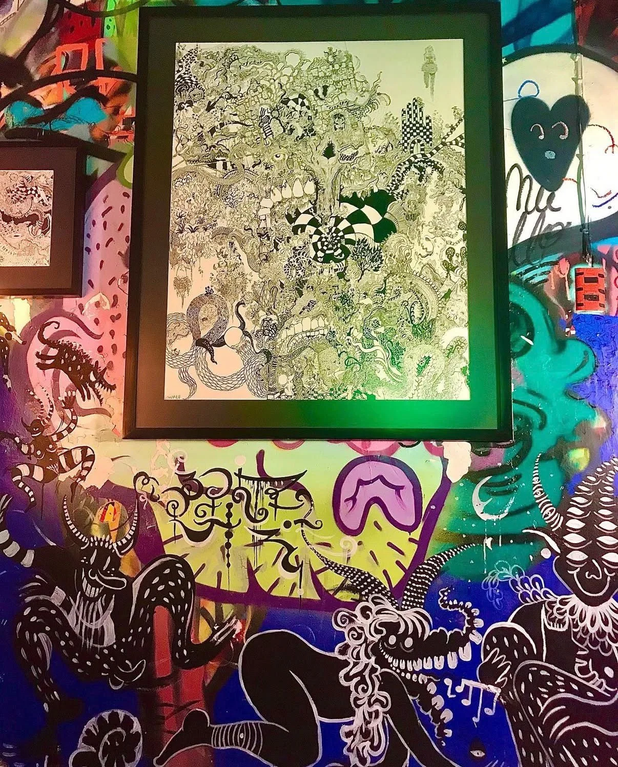 Imagen que muestra una pintura y un mural colorido con arte abstracto y dibujos de criaturas fantásticas en un espacio decorado con neón.