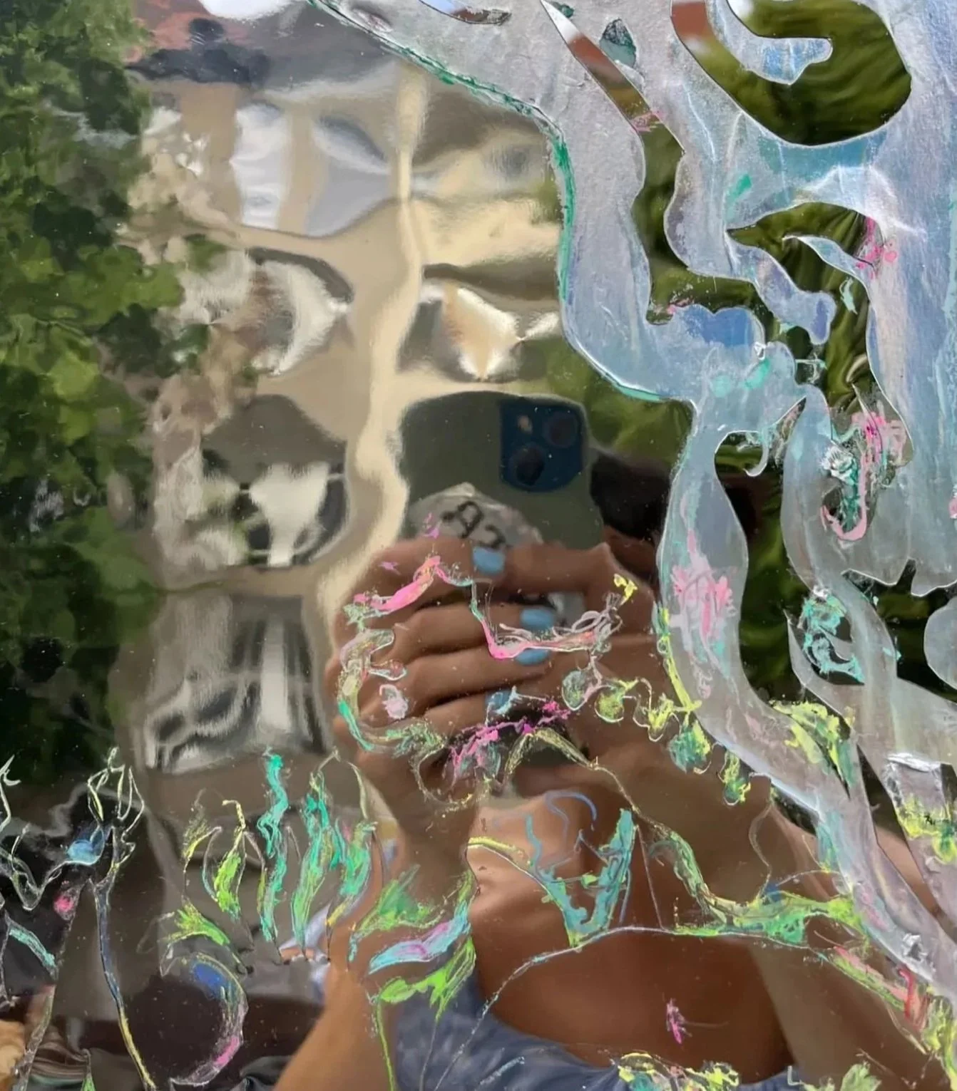 Reflejo de una persona tomando una selfie en un espejo cubierto con pintura de colores y marcas