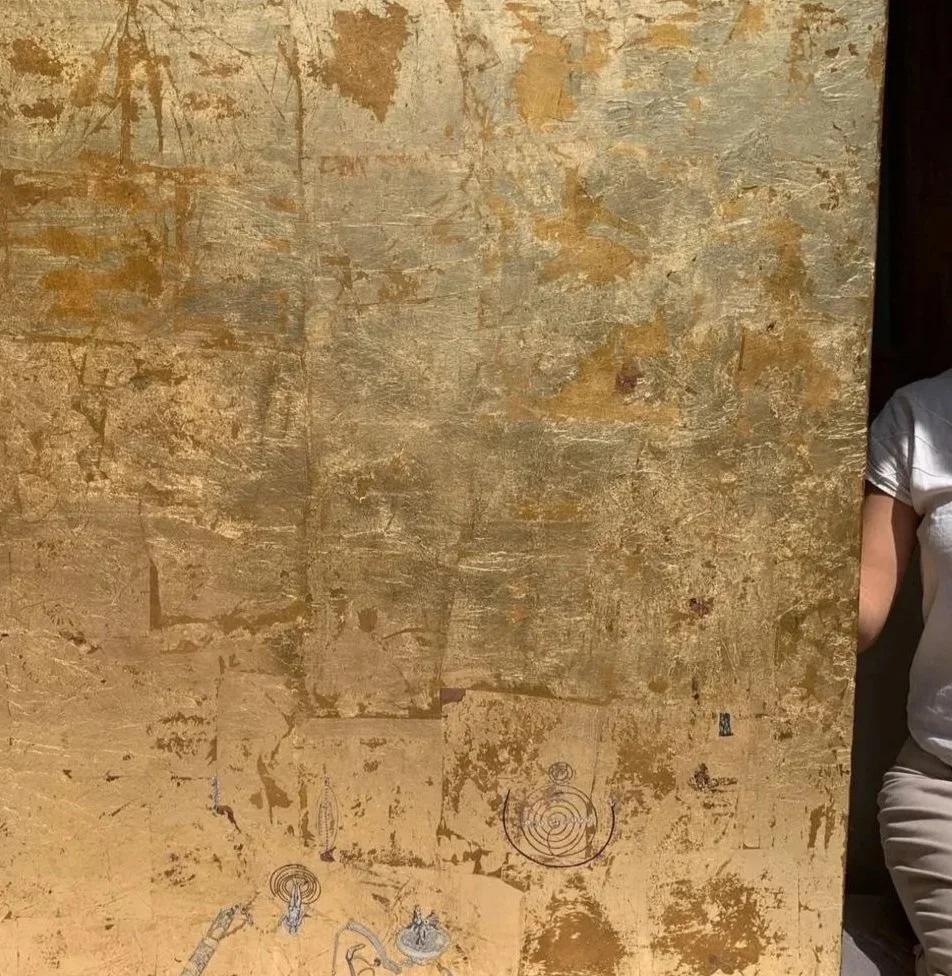 Pared de color beige con textura desgastada y marcas, con algunos dibujos en la parte inferior, y una persona parcialmente visible a la derecha, usando una camiseta blanca.