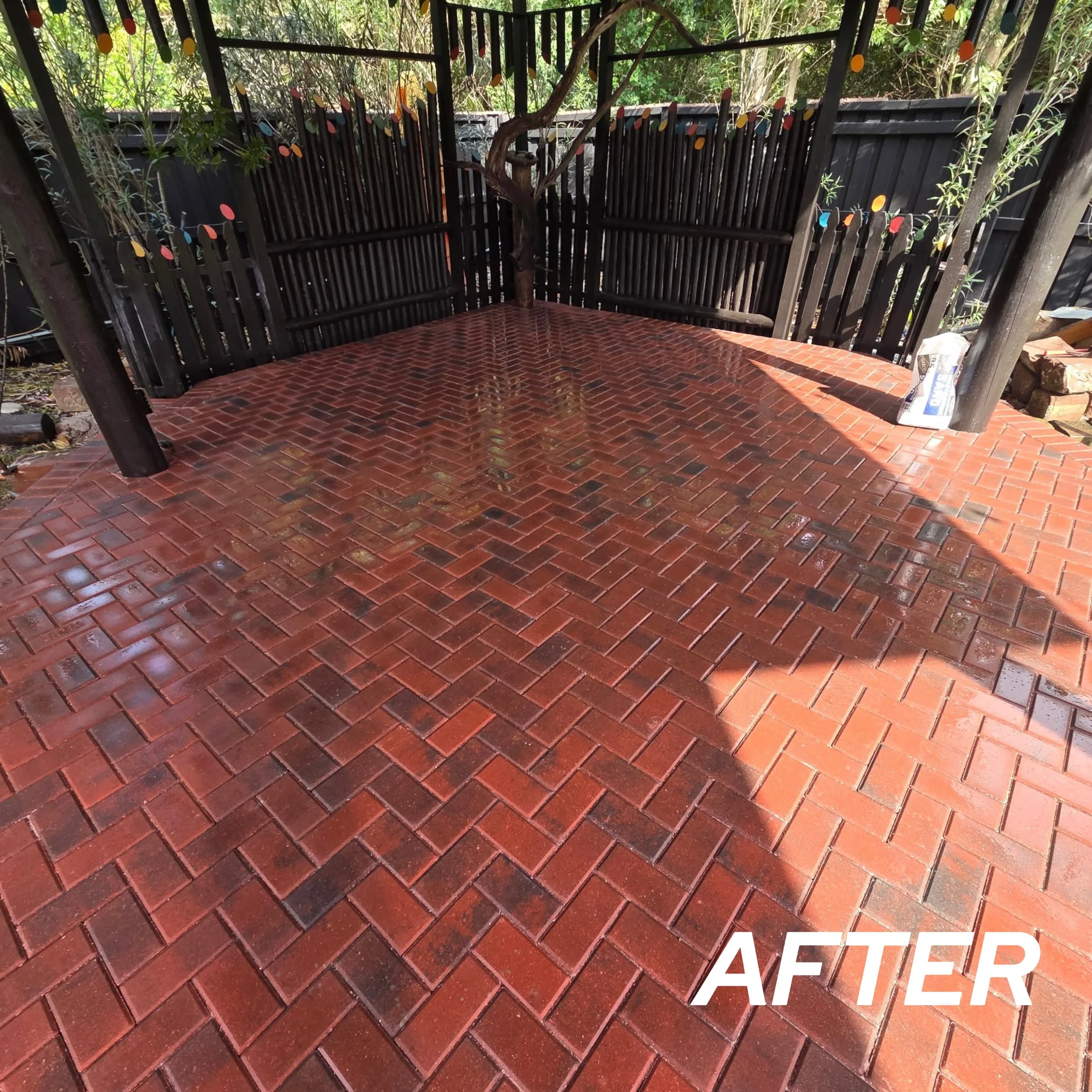 Clean, wet red brick patio with a black wooden fence and string lights, featuring a small tree and a bag of grout or cleaning supplies, labeled as 'AFTER'.