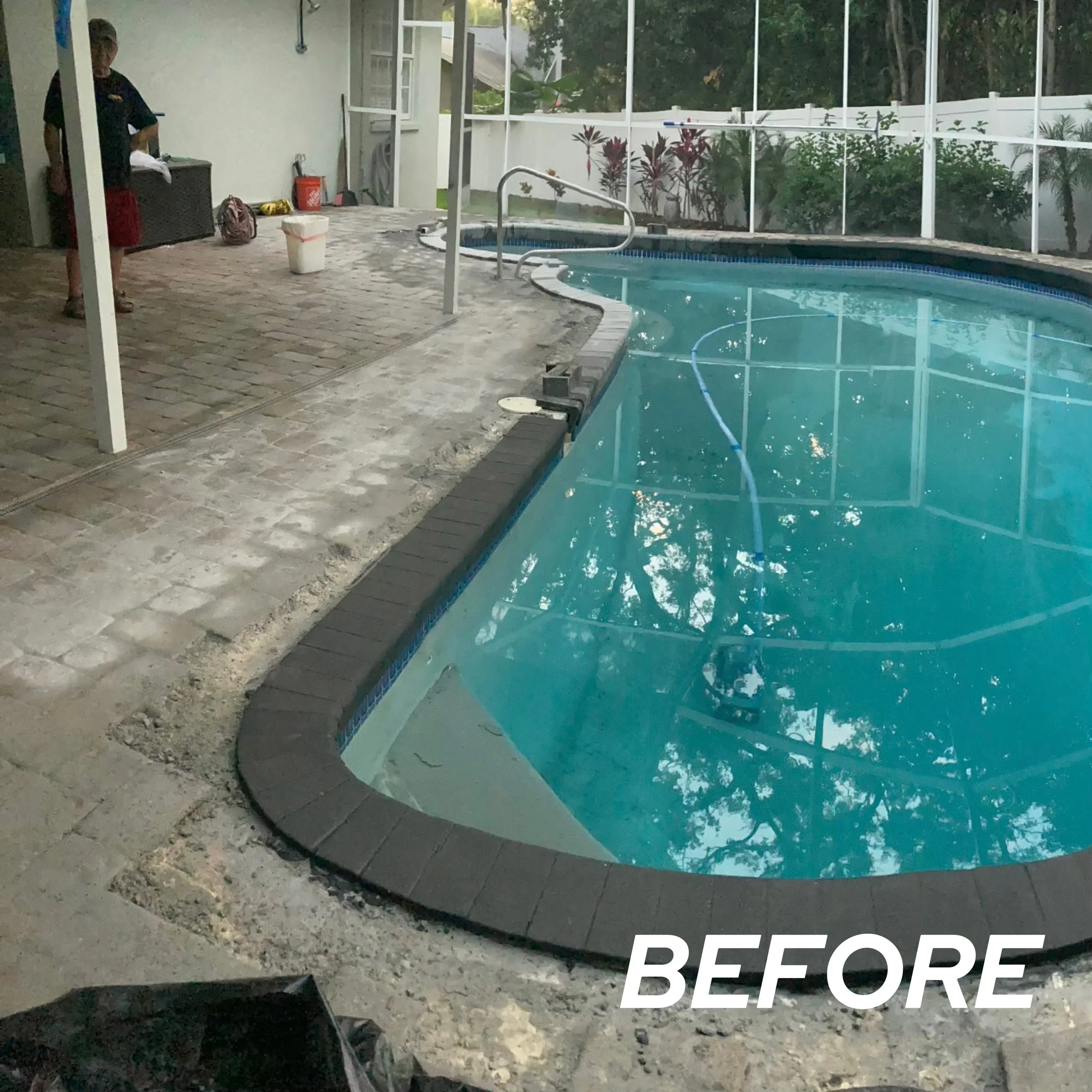In-ground swimming pool with a spa, surrounded by a brick and stone patio, with pool cleaning equipment visible and an enclosure with mesh screen and plants outside.