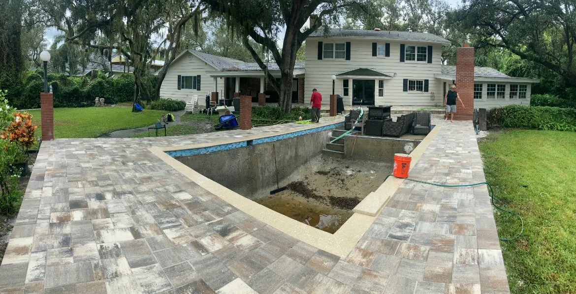 Backyard with a house, a patio, and an empty swimming pool under renovation.