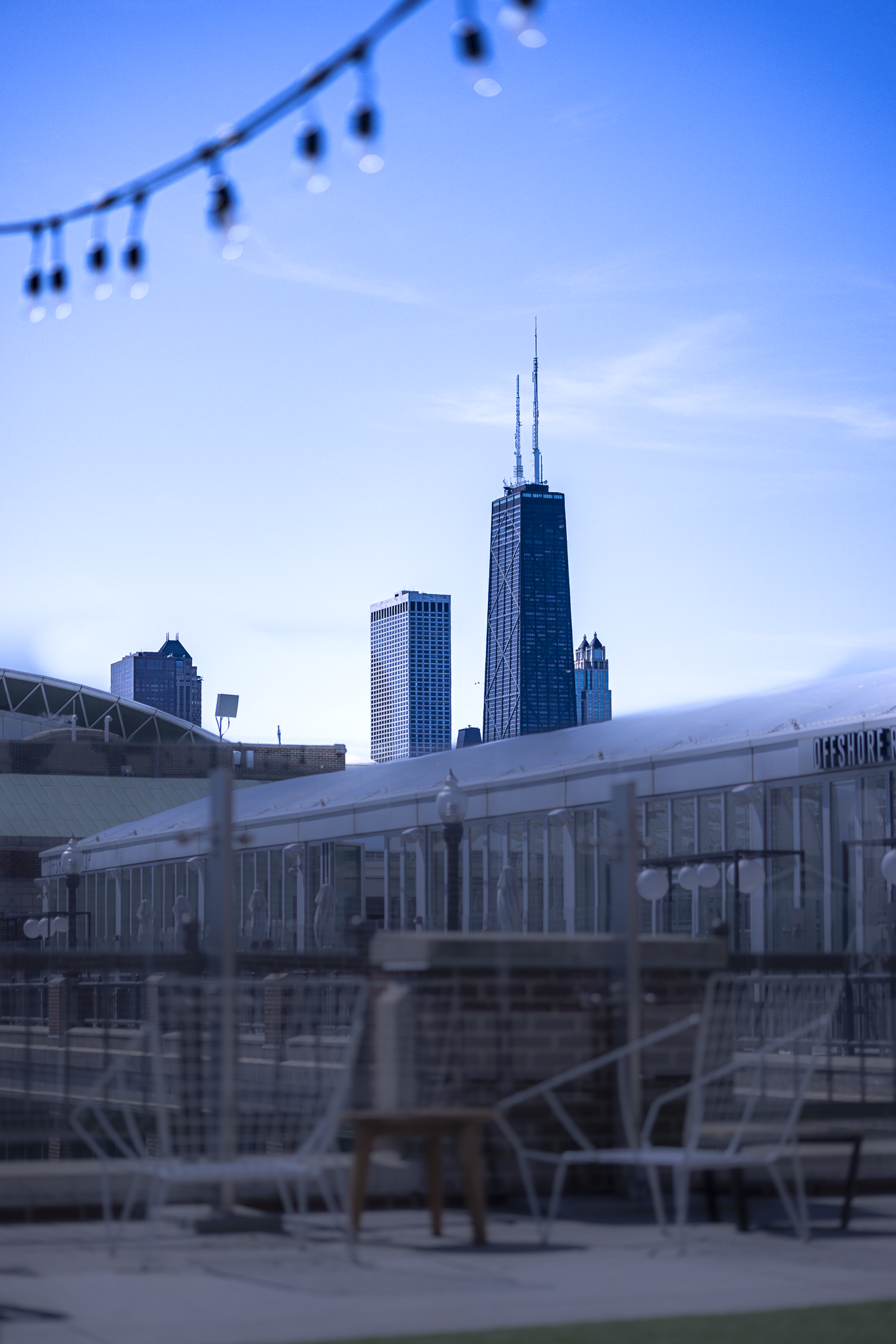 City skyline with prominent skyscraper and outdoor seating area with string lights in the foreground.