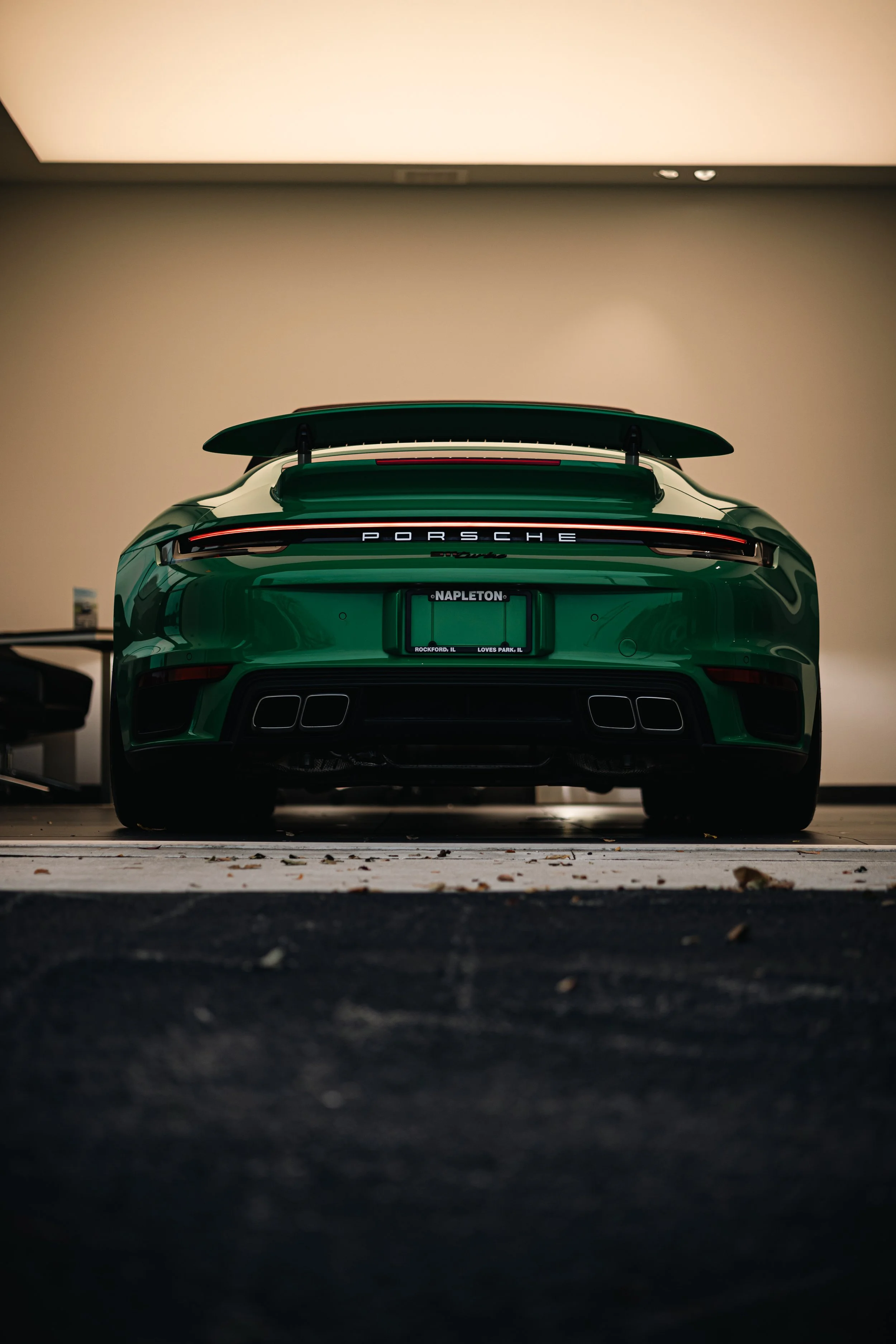 Green Porsche 911 Turbo parked indoors, viewed from the rear.